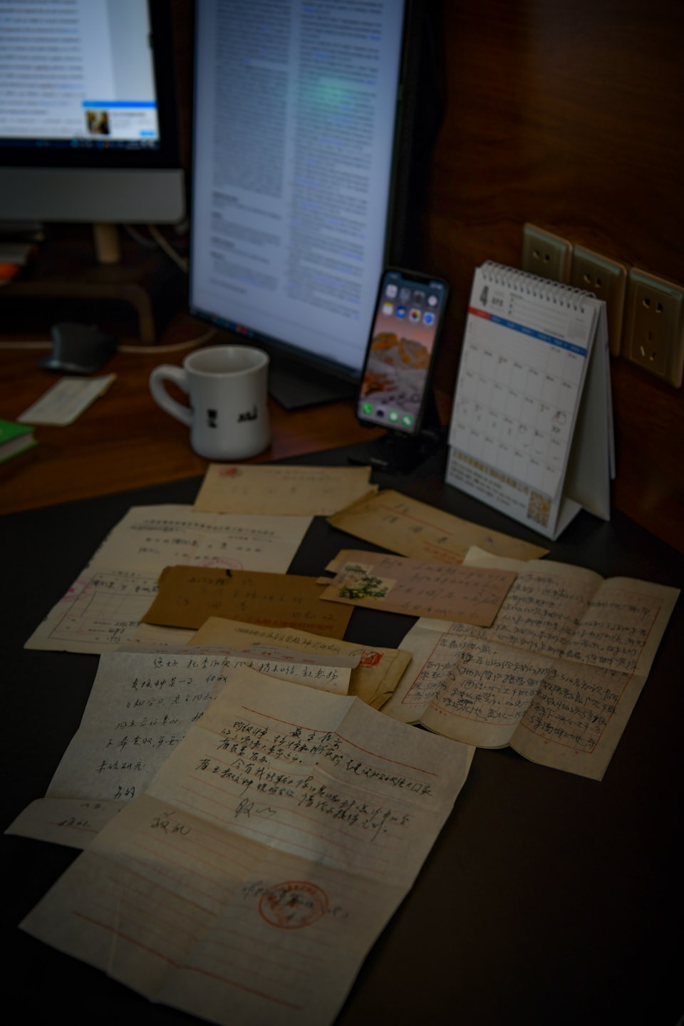 Handwritten historical documents rest on a desk with modern technology.
