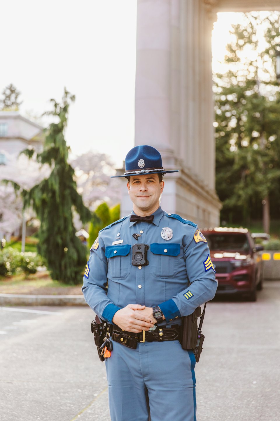Police officer in uniform standing outdoors near architectural columns.