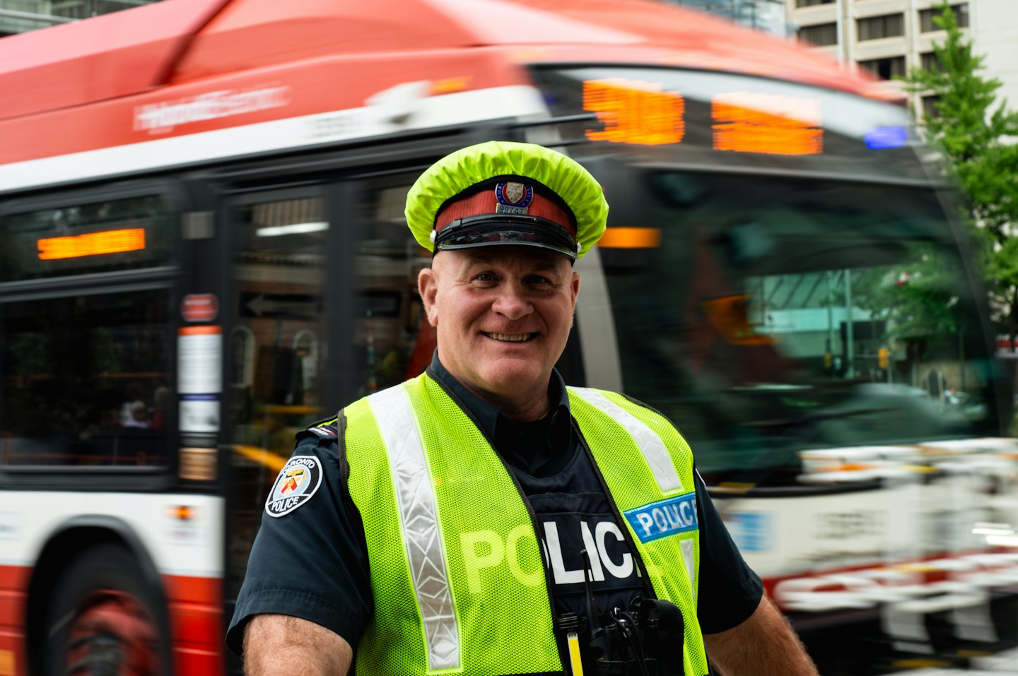 Smiling police officer in reflective vest stands by a bus.